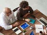 Mensen werken aan tafel met laptops en notitieboeken.